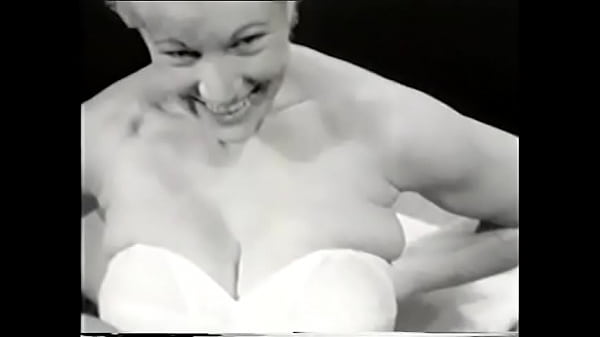 Sexy blonde in a white corset poses for the camera exposing her big tits to a photographer from the 60s for a men's magazine